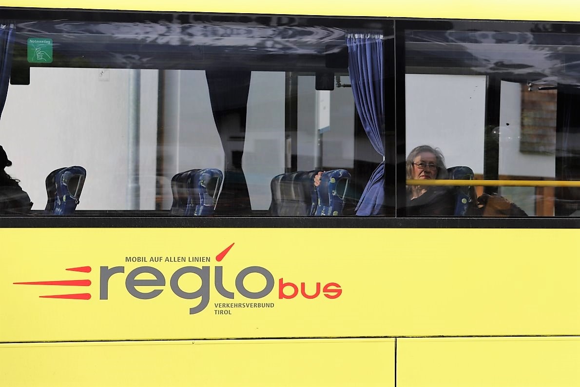 Ein Regio-Bus hält an der Bushaltestelle. Die Passagiere beobachten während des Halts amüsiert das bunte Treiben.